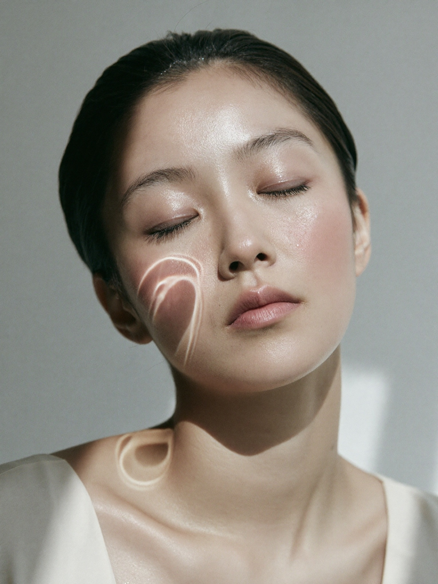 A woman with luminous hydrated skin, eyes closed, water-caustic light across her cheek