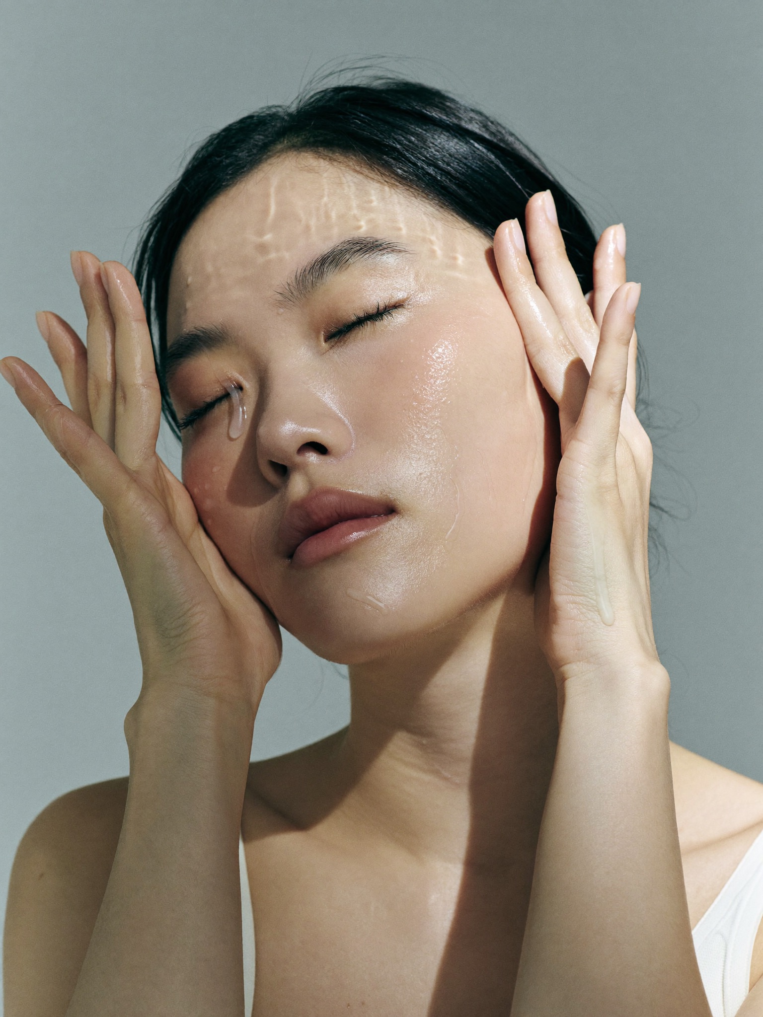 A woman pressing treatment essence into her cheeks with both palms