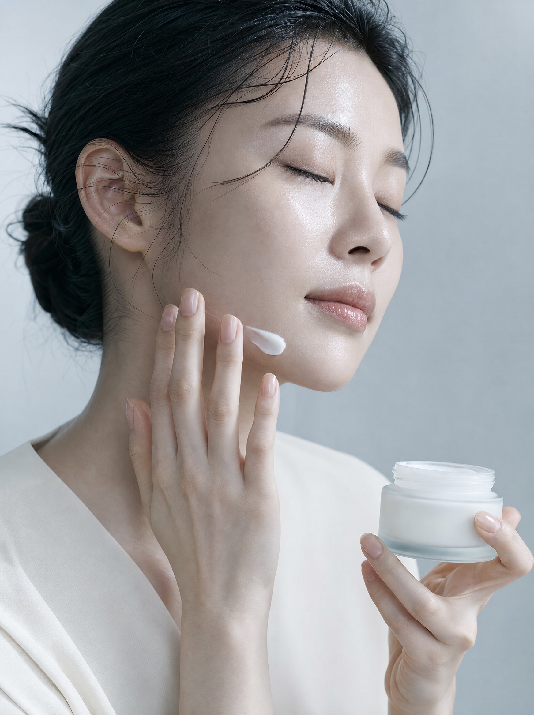 Fingertips drawing a trail of white cream along a woman's jawline