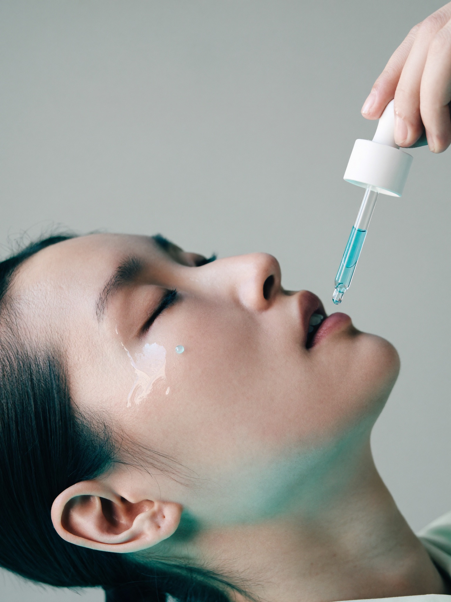 A serum dropper holding one drop above a woman's cheekbone